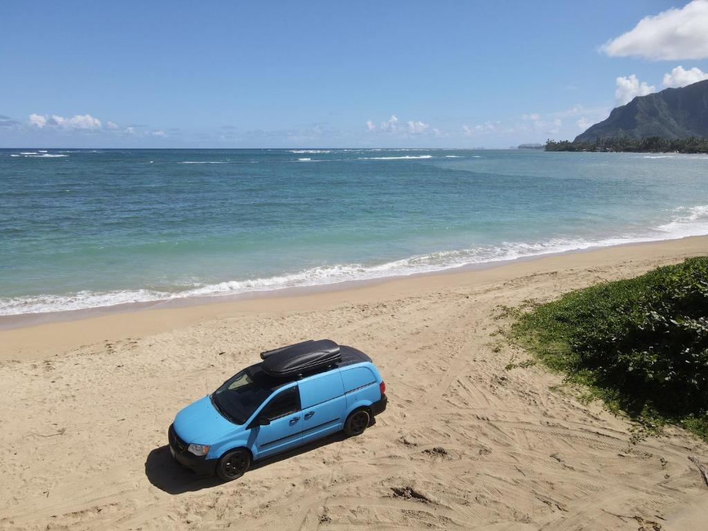 a blue car parked on a beach next to the ocean at HW Campervan Rental NO CAMPGROUND in Hauula