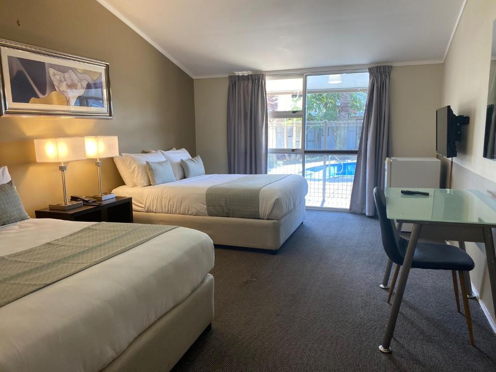 a hotel room with two beds and a desk and a window at Airport Gateway Hotel in Auckland