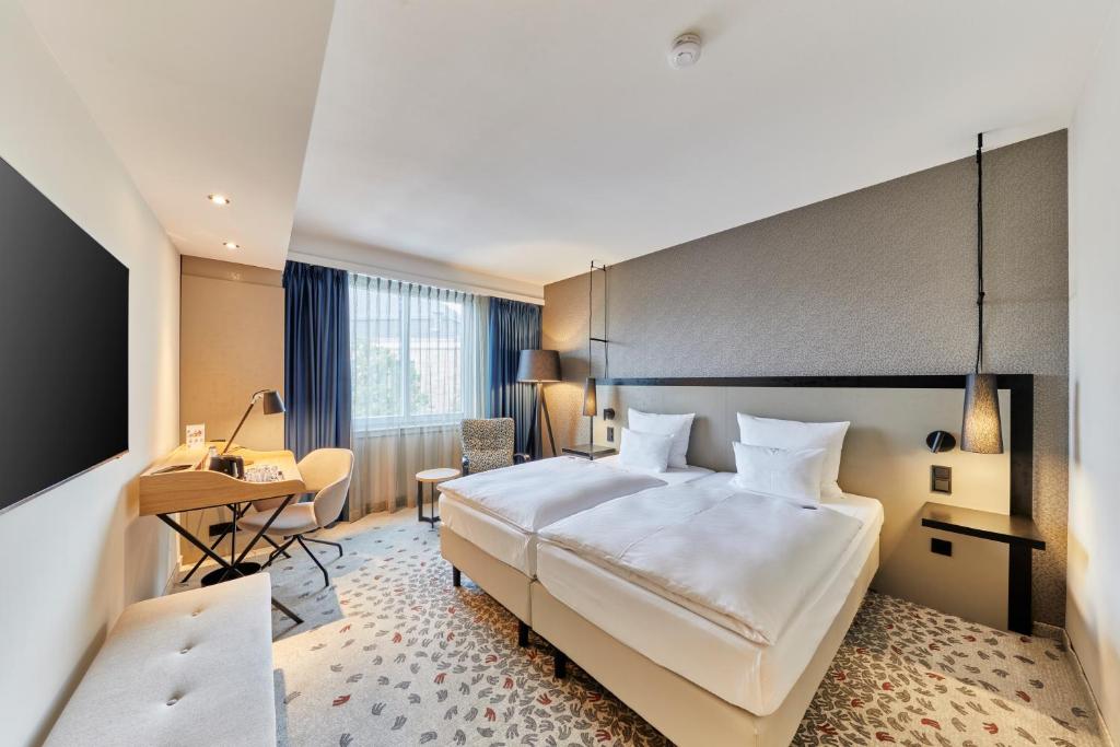 ein Hotelzimmer mit einem großen Bett und einem Schreibtisch in der Unterkunft Steigenberger Hotel Bielefelder Hof in Bielefeld