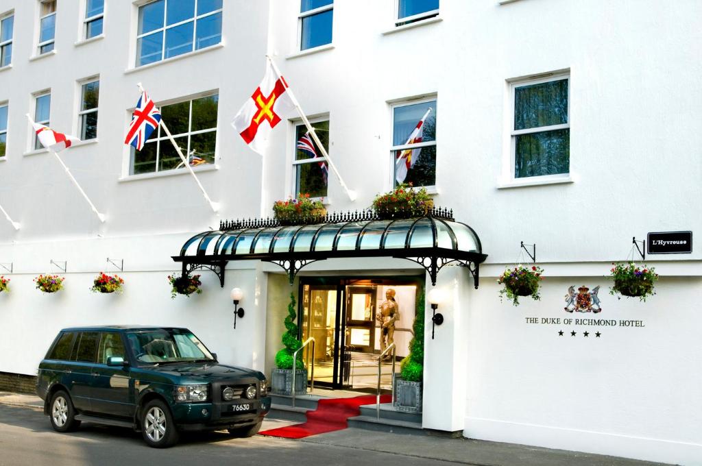 un coche aparcado fuera de un edificio con banderas británicas en Duke Of Richmond Hotel en St. Peter Port