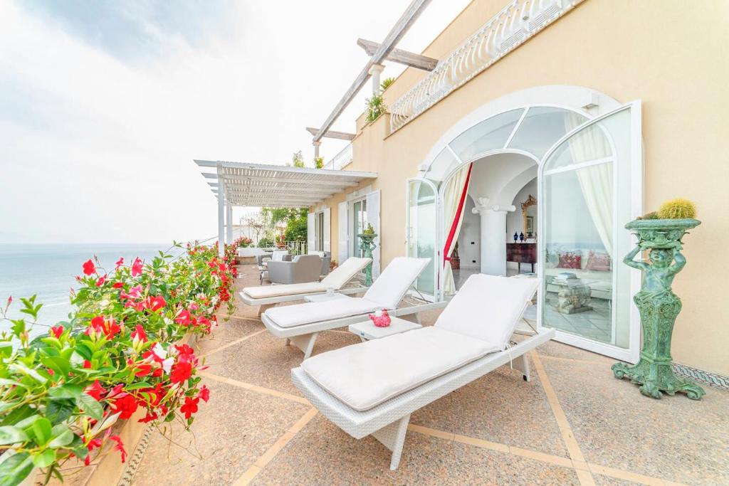 a patio with white chairs and flowers and the ocean at Amalfi coast-Praiano Villa Cristina no steps in Praiano