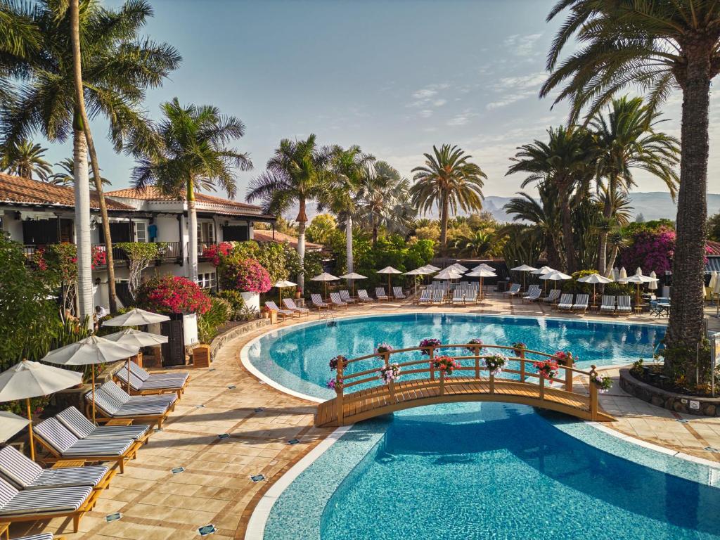 a pool at a resort with chairs and a bridge at Seaside Grand Hotel Residencia - Gran Lujo in Maspalomas