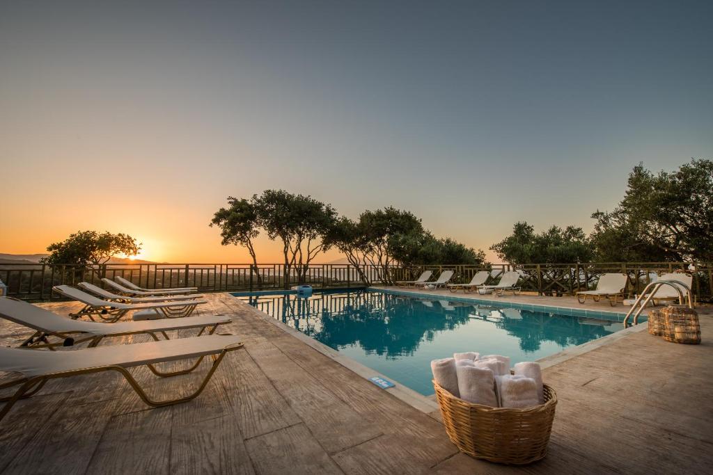 a swimming pool with chairs and a sunset in the background at Lofos Soilis in Tragaki