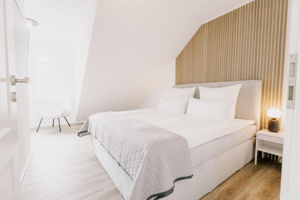 a white bedroom with a large bed with a wooden headboard at Küsten Suite de See - Suite 2 direkte Deichlage, Balkon, 77qm in Greetsiel