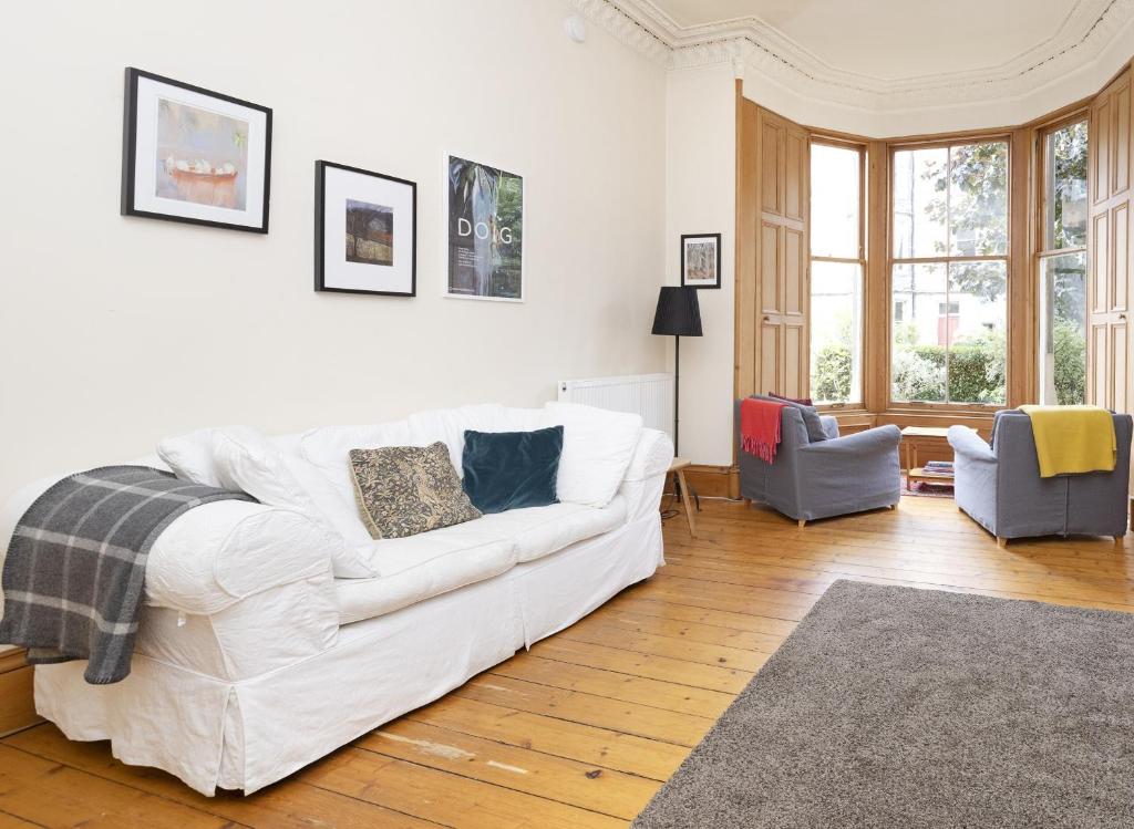 ALTIDO 3-bed Meadows flat near Castle في إدنبرة: غرفة معيشة مع أريكة بيضاء وكرسيين