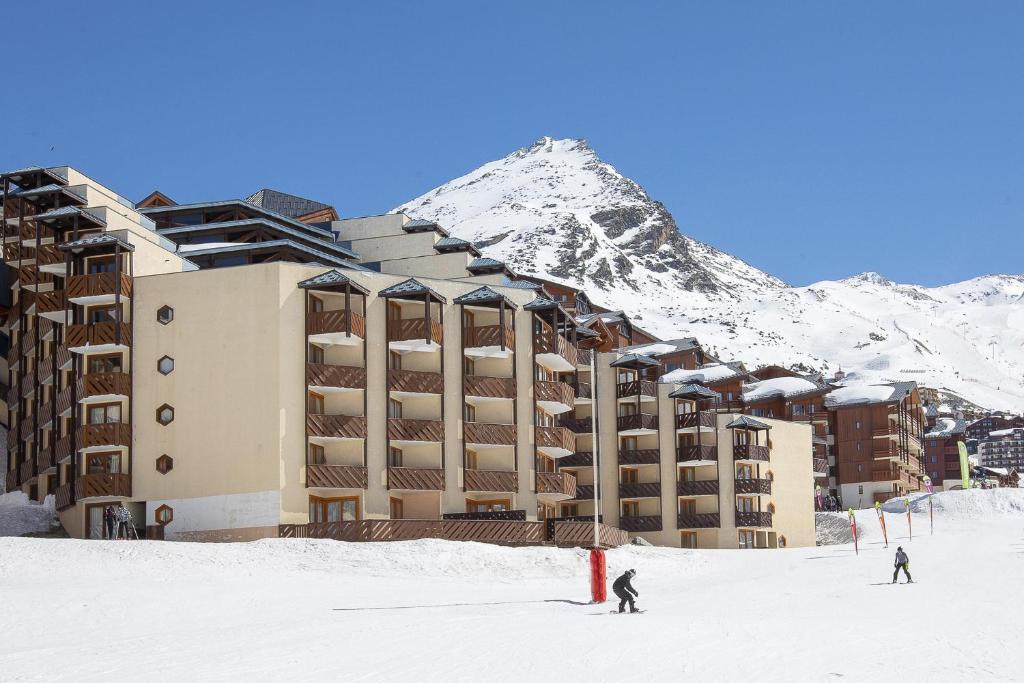 two people skiing in the snow in front of a hotel at Résidence & Spa Le Machu Pichu in Val Thorens