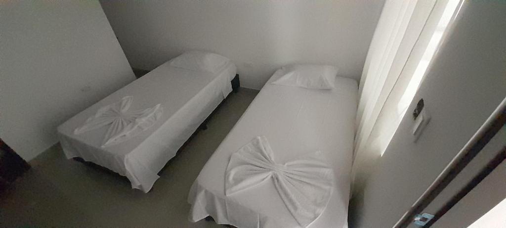 duas camas num pequeno quarto com lençóis brancos em Hotel Apartado Real em Apartadó