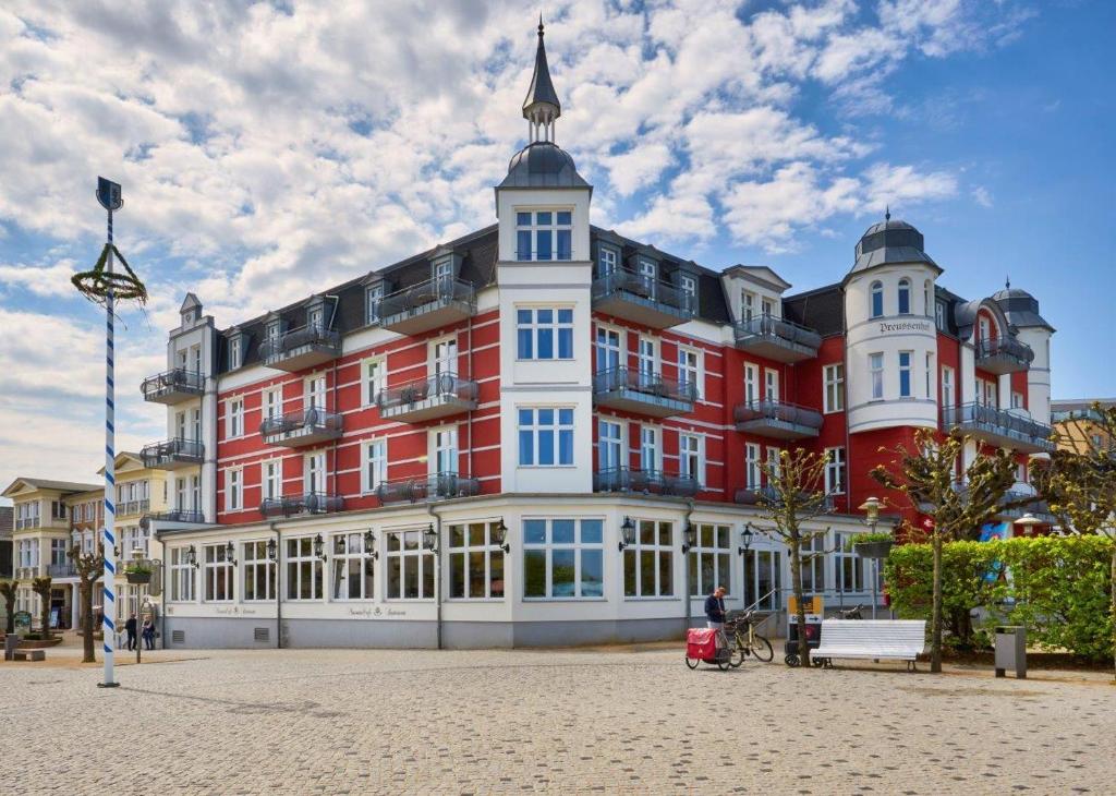 un grand bâtiment rouge et blanc avec une personne assise devant lui dans l'établissement Strandhotel Preussenhof, à Zinnowitz