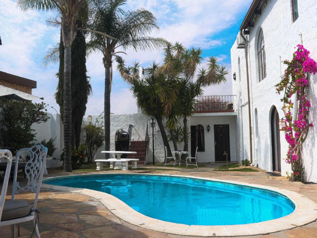 a swimming pool in front of a house with palm trees at Casa Blanca Boutique Hotel Pension in Windhoek