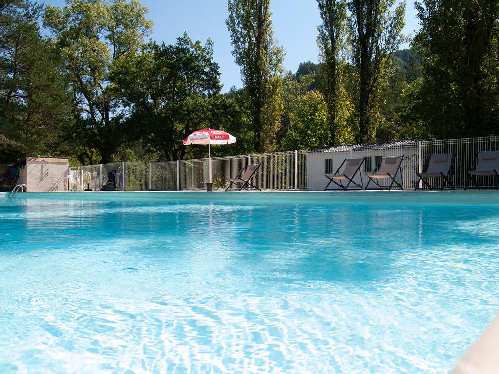 a large swimming pool with an umbrella and chairs at Camping L'Ondine de Provence in La Motte-Chalançon