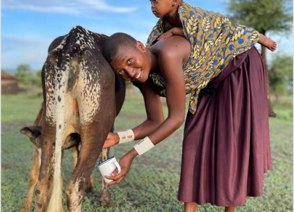 una mujer sosteniendo un niño en la espalda de una vaca en Mombo Maasai Culture Homestay, 