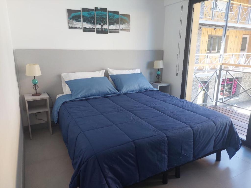 Cama azul en habitación con ventana grande en Tu lugar en Loretta 4 en San Martín de los Andes