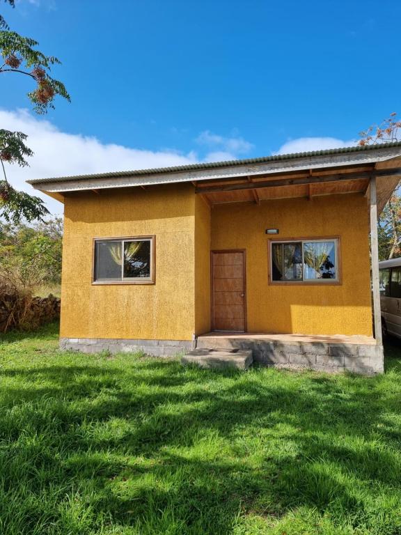 ein kleines gelbes Haus mit einem Rasenhof in der Unterkunft Mika's House 2 in Hanga Roa