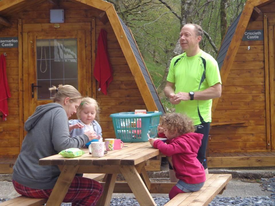 a man and two girls at a picnic table in front of a cabin at Bryn Dinas Camping Pods Ltd. in Beddgelert