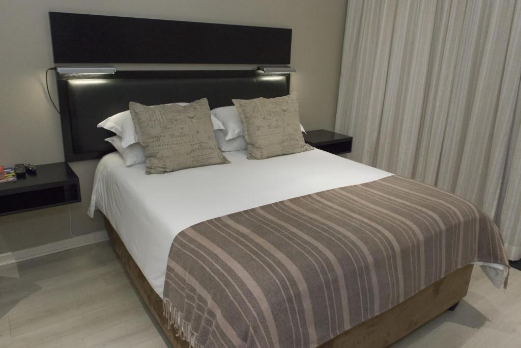um quarto com uma cama grande com lençóis brancos e almofadas em The Suburban Guest House em Bloemfontein
