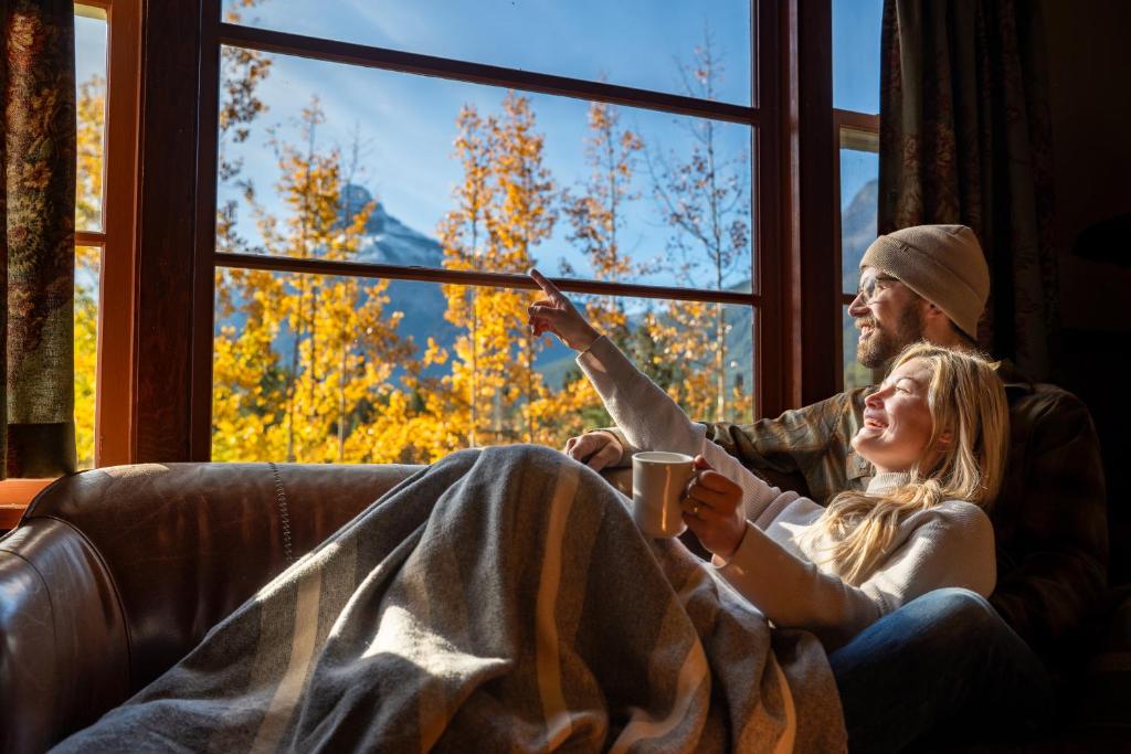un homme et une femme assis sur un canapé donnant sur une fenêtre dans l'établissement Johnston Canyon Lodge & Bungalows, à Castle Junction