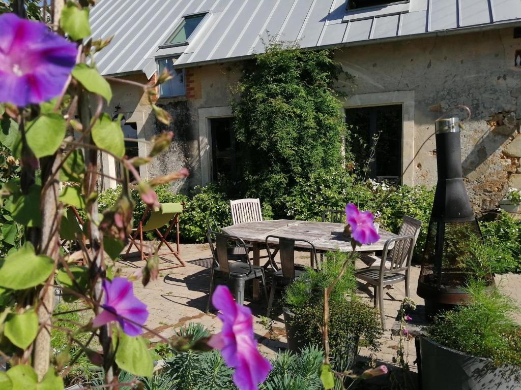 a patio with a table and chairs and purple flowers at Les chambres de balade au jardin in Épineu-le-Chevreuil