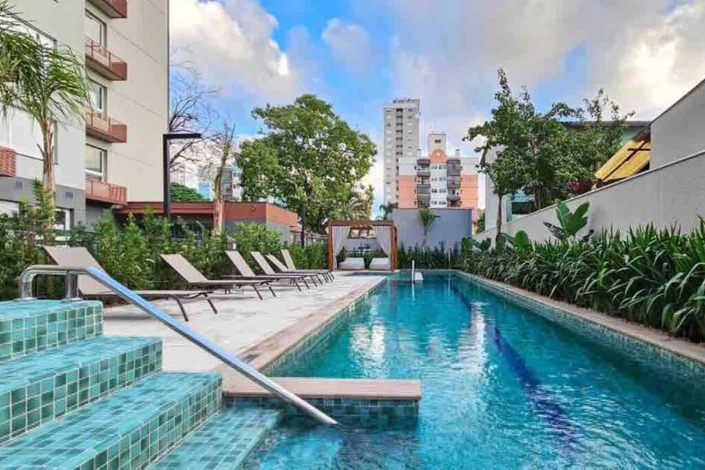 a swimming pool with chairs and a building at Apto Vilage Puc in Porto Alegre