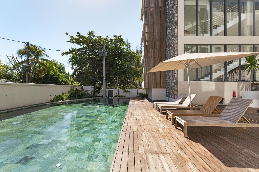 a pool with chairs and an umbrella next to a building at One Bay Penthouse in Grand Baie
