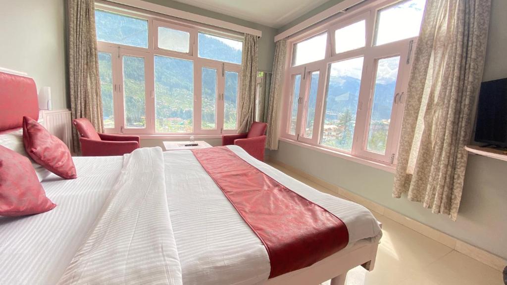 a bedroom with a large bed with windows at Hotel Mountain Meadows in Manāli