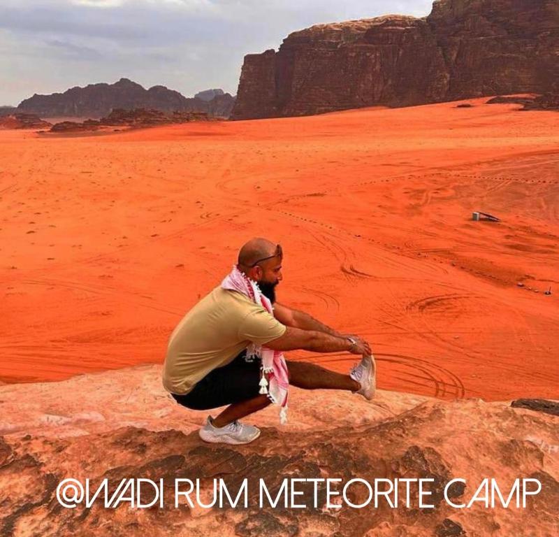 mężczyzna siedzący na kamieniu na pustyni w obiekcie Wadi Rum Meteorite camp w mieście Wadi Rum