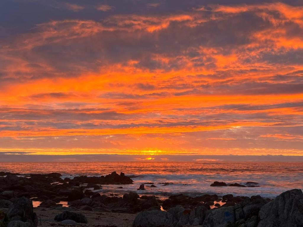 - un coucher de soleil sur une plage avec des rochers et l'océan dans l'établissement FRENTE AL MAR SUN & WAVES atardeceres mágicos, à Algarrobo
