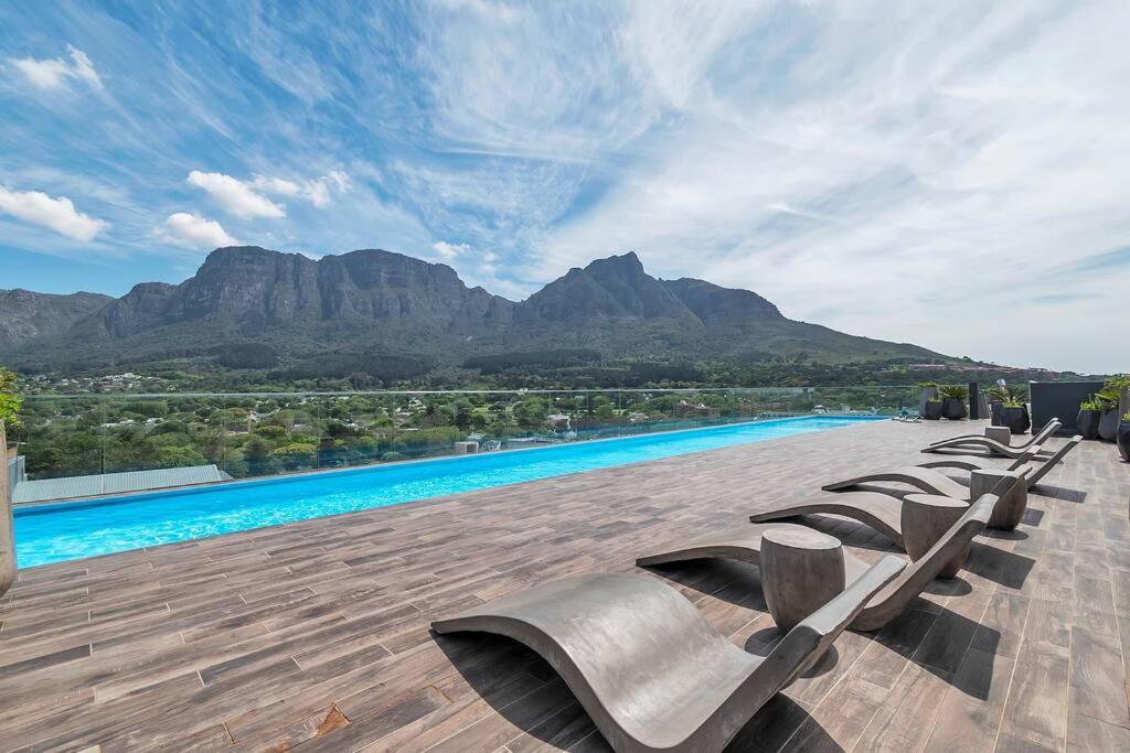 a row of chaise lounge chairs on a patio with mountains at Rooftop with breathtaking views of Table Mountain. in Cape Town
