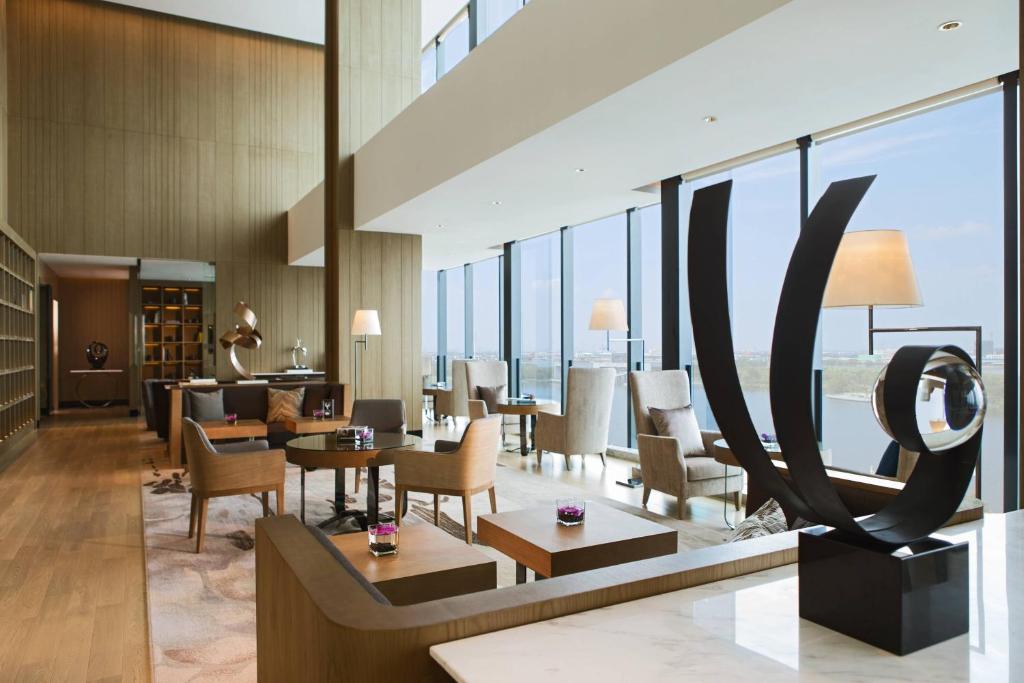hol hotelowy ze stołami i krzesłami oraz dużymi oknami w obiekcie Renaissance Suzhou Wujiang Hotel w mieście Suzhou
