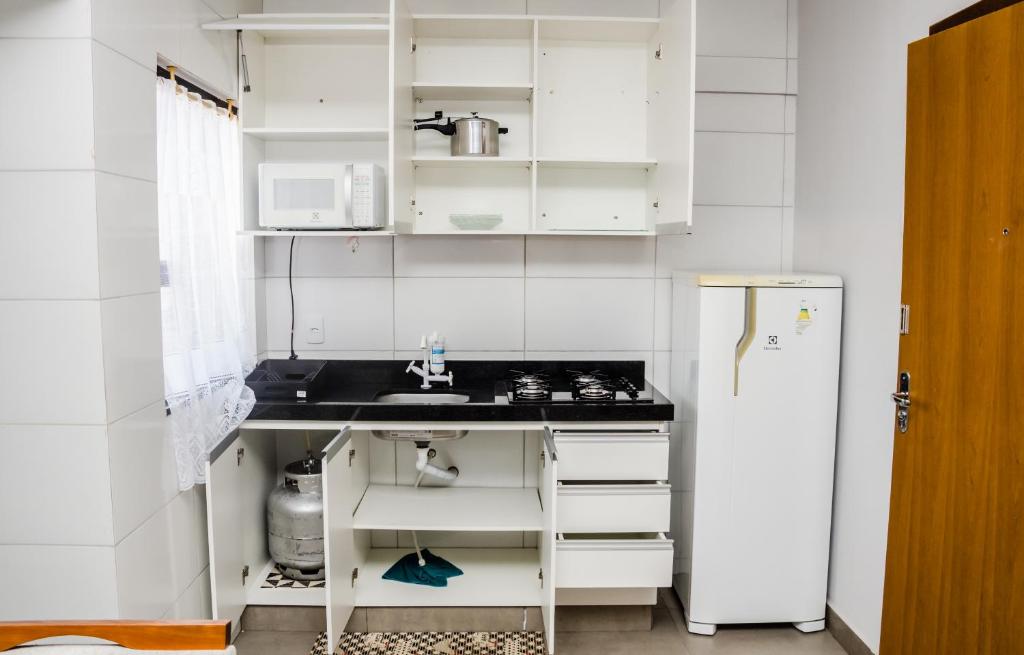 La cuisine blanche est équipée d'un évier et d'un réfrigérateur. dans l'établissement Apt 1 qto wifi - netflix - ar condicionado - prox ao metrô -ambiente familiar., à Ceilândia