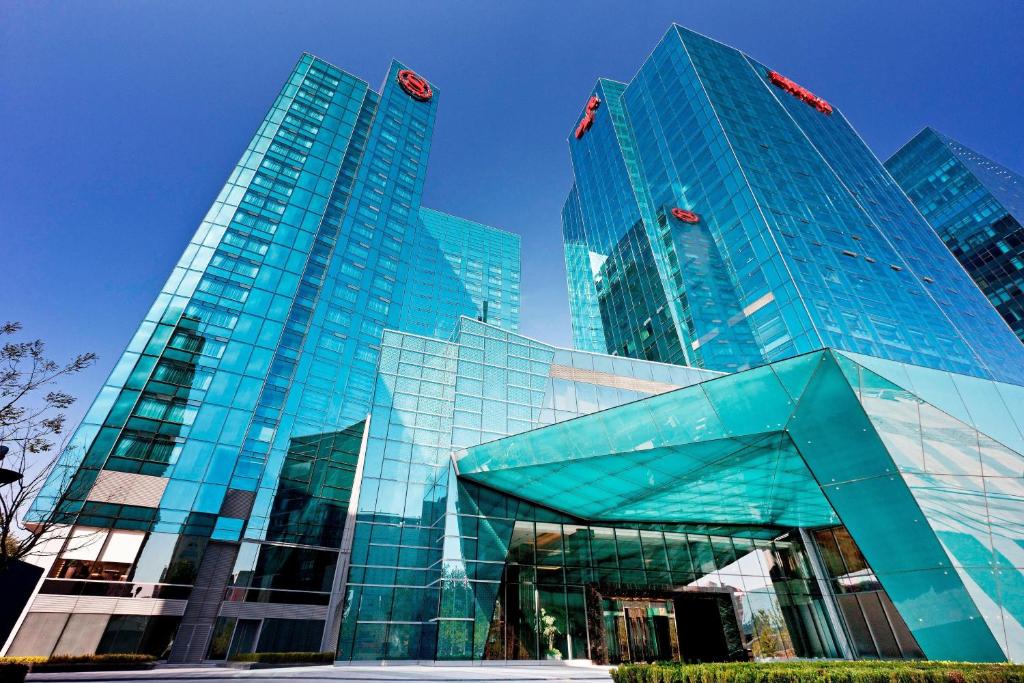 a large glass building with two tall buildings at Sheraton Grand Beijing Dongcheng Hotel in Beijing