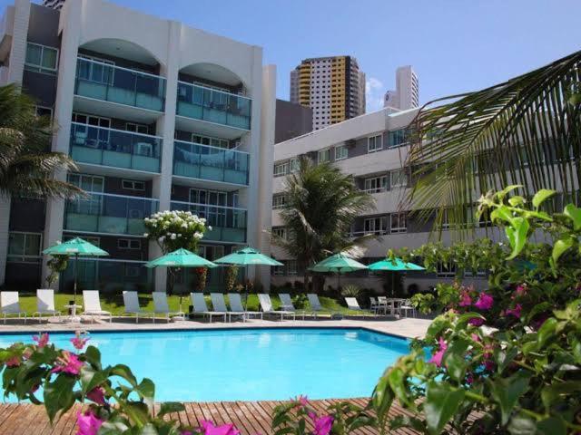 a swimming pool with chairs and umbrellas in front of a building at Ponta Negra Beach luxury hotel in Natal