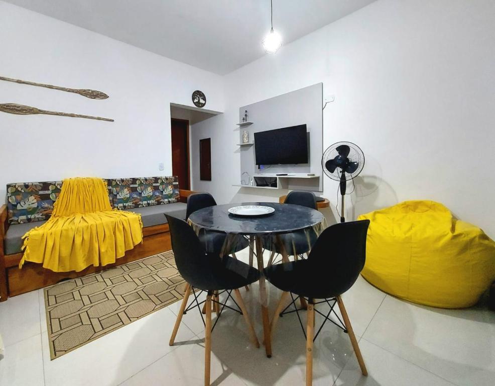 uma sala de estar com uma mesa e um sofá amarelo em Apartamento Ubatuba Maranduba 150m da Praia em Ubatuba