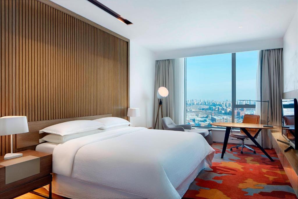 a bedroom with a bed and a desk and a large window at Four Points by Sheraton Changchun Hi-Tech Zone in Changchun