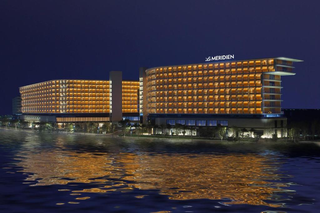 Le Méridien Xiaojing Bay في هويزو: فندق سانتا في الليل بجوار جسم من الماء