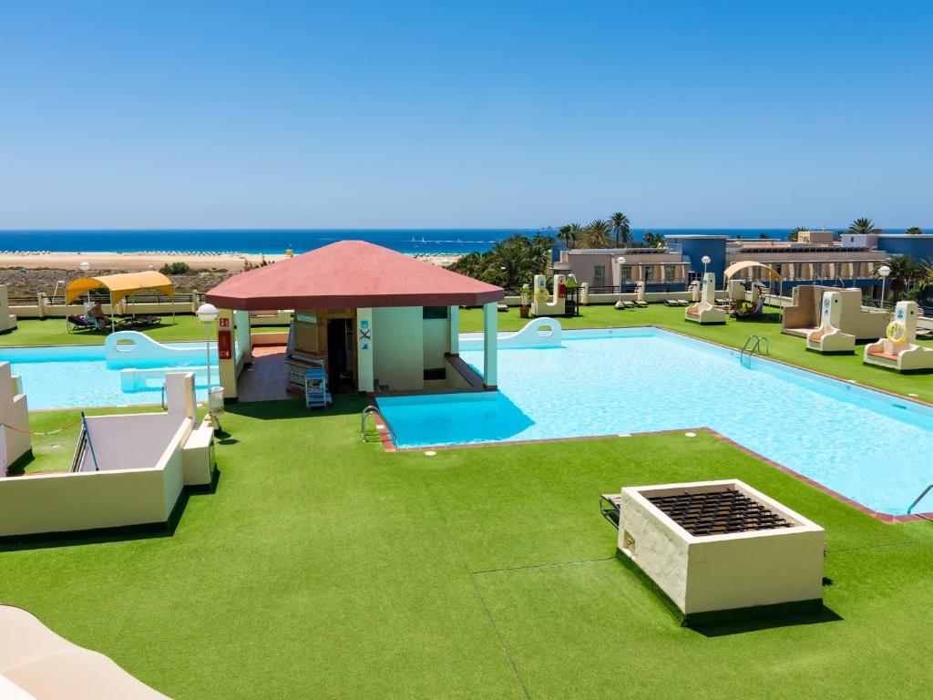 a large swimming pool with green grass and a resort at Matorral Beach Apartament beautiful ocean view in Morro del Jable