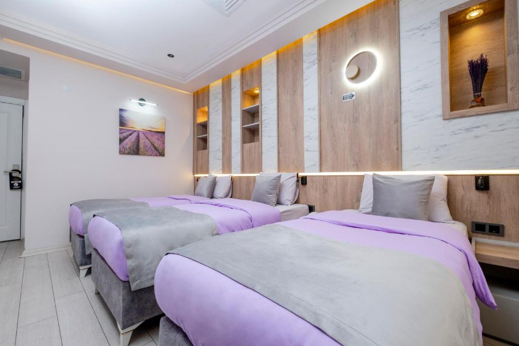 three beds in a room with purple sheets at Lavender Airport Hotel in Arnavutköy