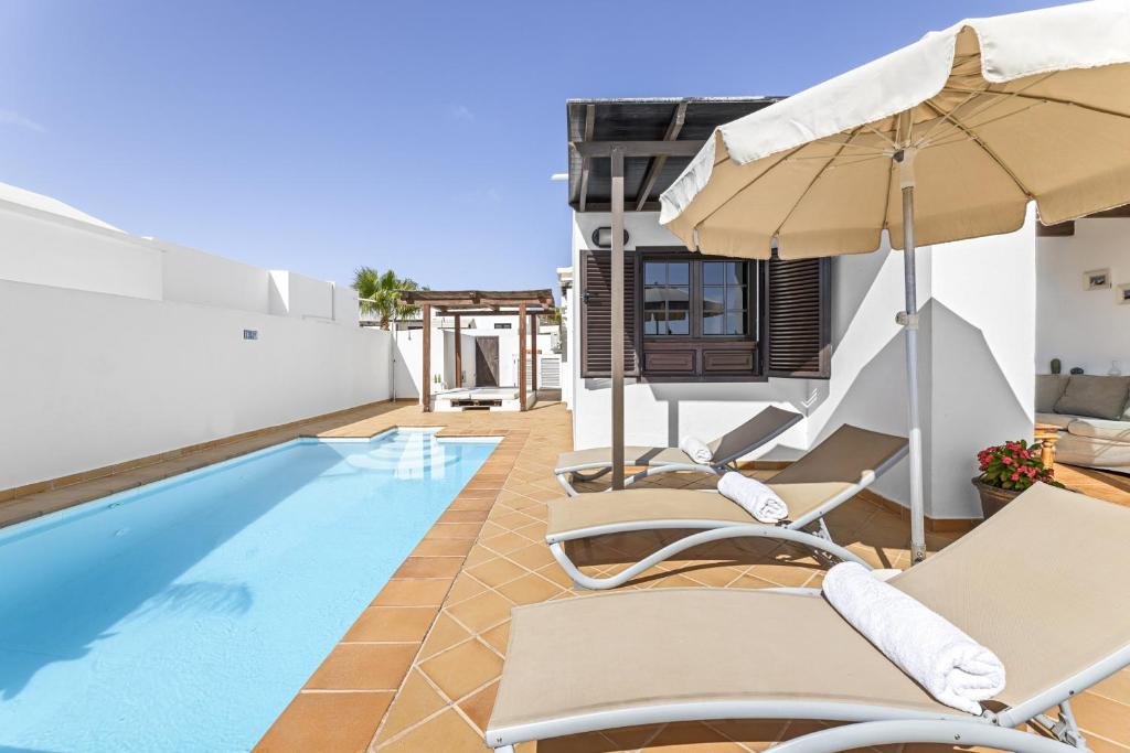 uma villa com uma piscina, cadeiras e um guarda-sol em Villa 6 - Villasexperience em Tías