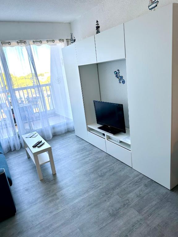 a white living room with a tv and a table at Studio vue port, parking privé, terrasse, clim in Le Grau-du-Roi