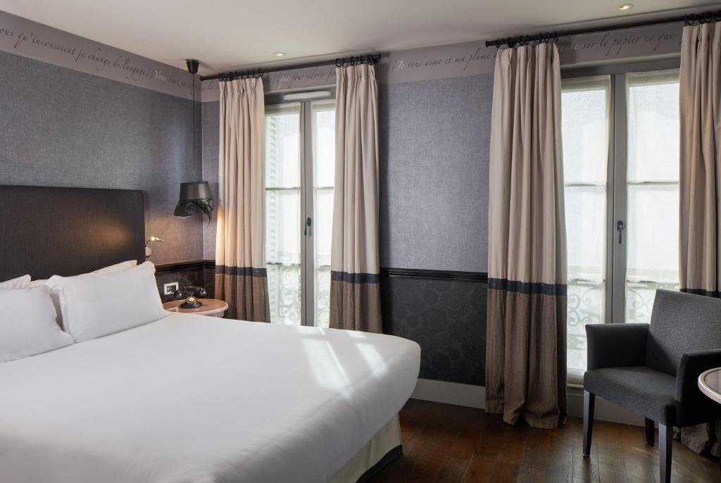 ein Hotelzimmer mit einem Bett, einem Stuhl und Fenstern in der Unterkunft Les Plumes Hotel in Paris