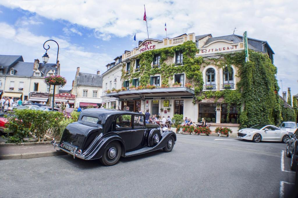 un viejo coche negro conduciendo por una calle de la ciudad en Logis Hotel De France, en La Chartre-sur-le-Loir