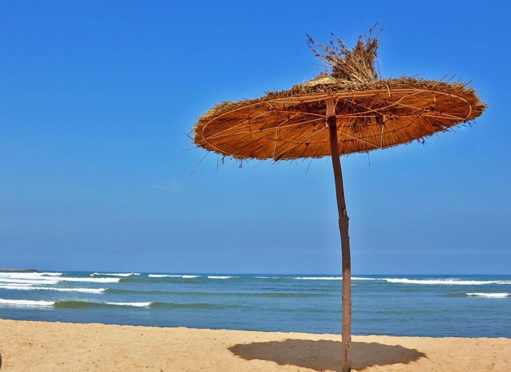 a straw umbrella on a beach with the ocean at Apparemment de luxe Bouznika in Bouznika