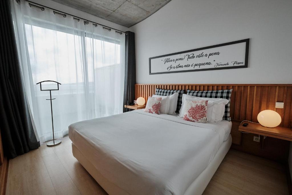 a bedroom with a large white bed and a window at Hotel Praia Marina by RIDAN Hotels in Praia da Vitória