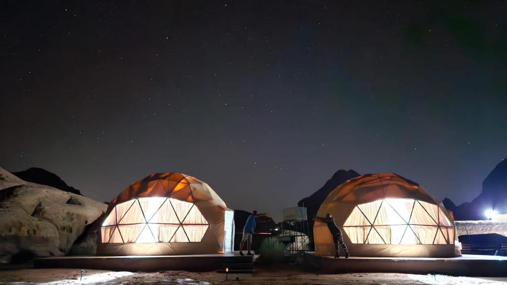 two domes are lit up at night under the stars at مخيم الجبال البرونزية in Wadi Rum