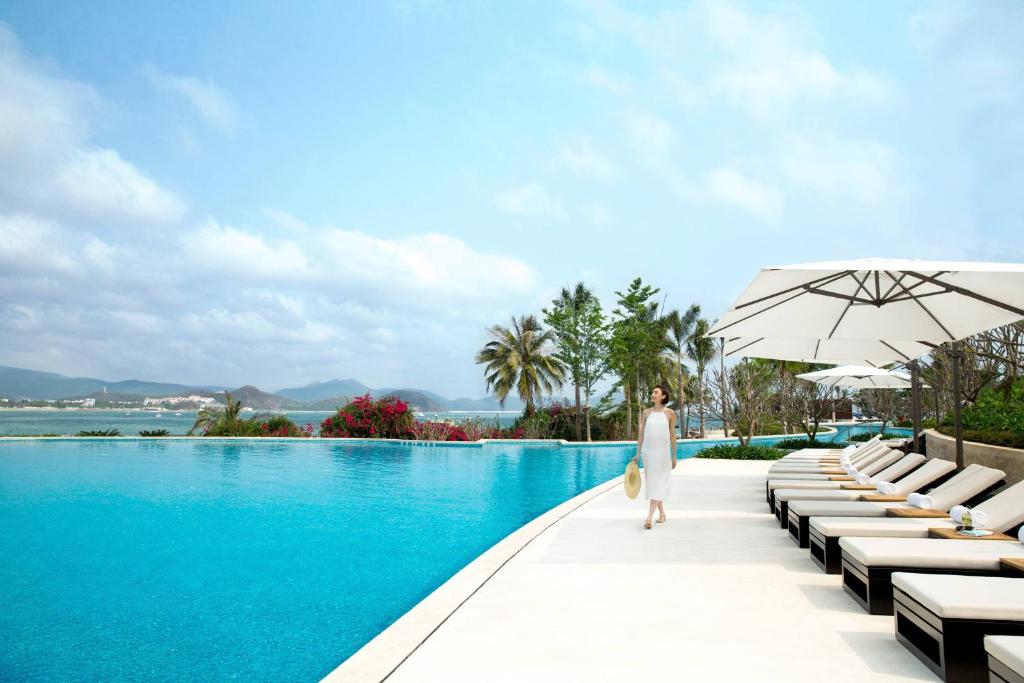 Eine Frau in weißem Kleid steht neben einem Pool in der Unterkunft JW Marriott Hotel Sanya Dadonghai Bay in Sanya