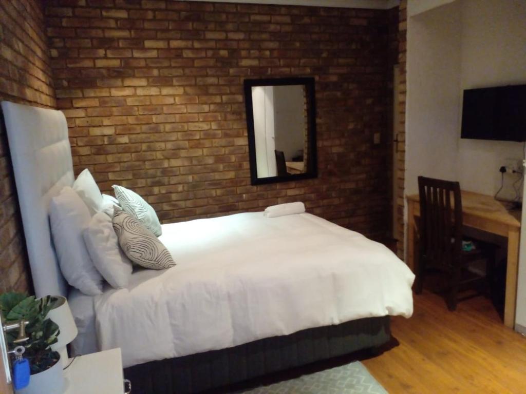 a bedroom with a white bed and a brick wall at Tshidiso Guesthouse in Centurion