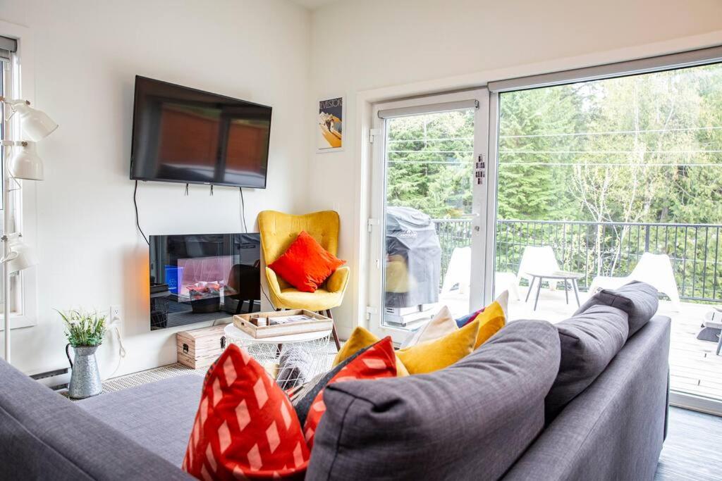 a living room with a gray couch with red and yellow pillows at Reved Up & Out - Remarkable Two Bedroom Condo in Revelstoke