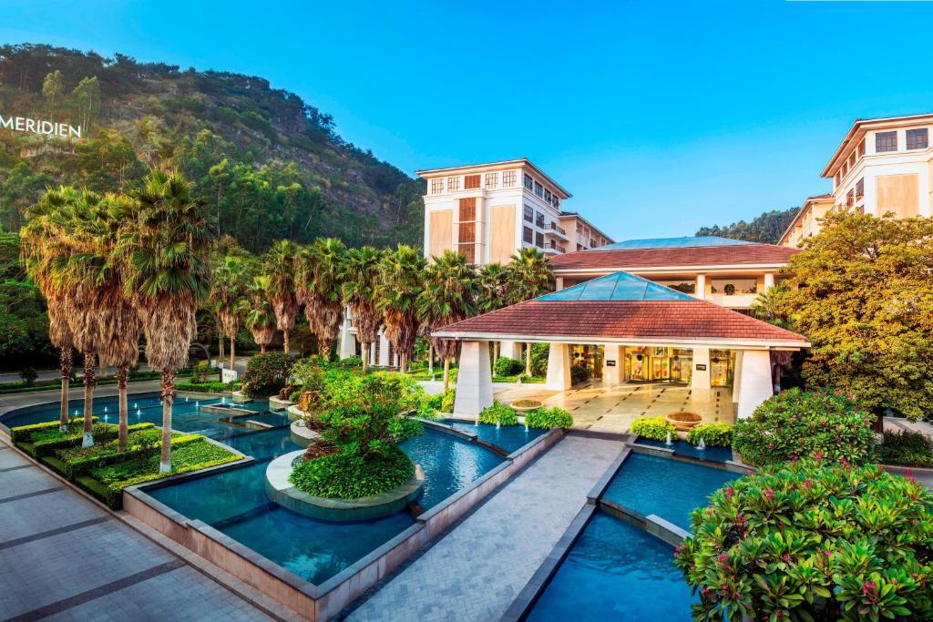 ein Resort mit einem Pool, Palmen und einem Gebäude in der Unterkunft Le Méridien Xiamen in Xiamen