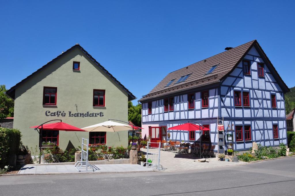 un par de edificios con sombrillas rojas delante en Café Landart im Thüringer Finistère en Plaue