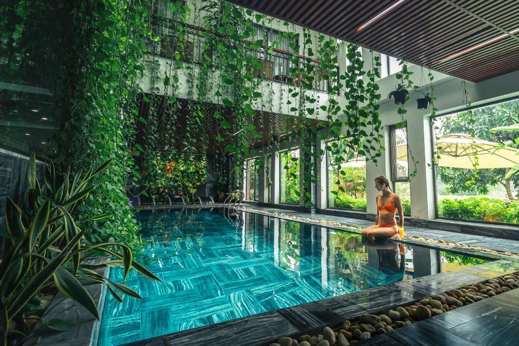 a woman sitting next to a swimming pool in a building at Liberty Hall Tam Coc Hotel & Villa in Ninh Binh