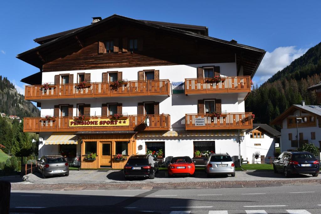 un grand bâtiment avec des voitures garées devant lui dans l'établissement Albergo Pensione Sport, à Arabba